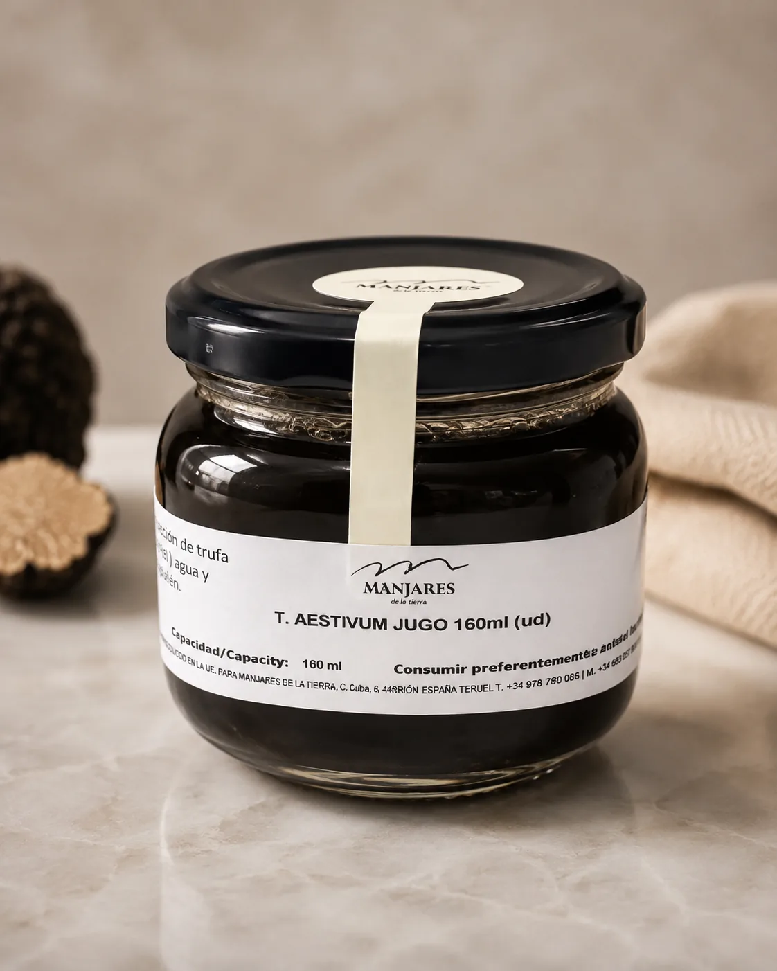 Manjares szarvasgombalé 160 ml-es üvegben világos márványon, mögötte fekete szarvasgomba és vászon
